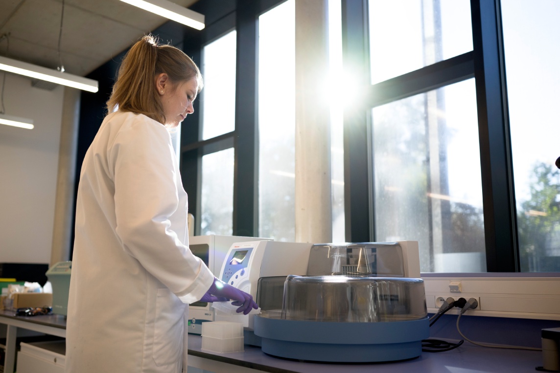 Scientist operating a benchtop instrument by a window.
