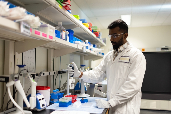 Scientist pipetting beside reagent storage shelves.