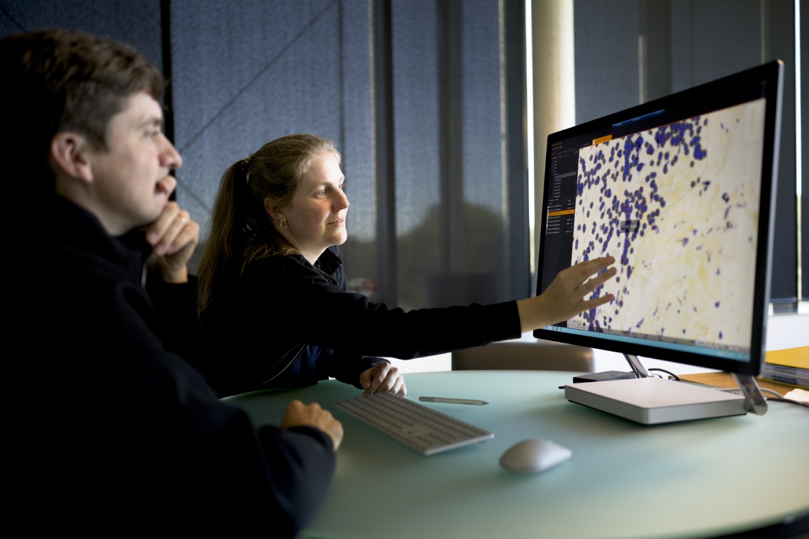 Pathologist and imaging scientist reviewing AI-assisted digital image analysis results on dual-monitor workstation