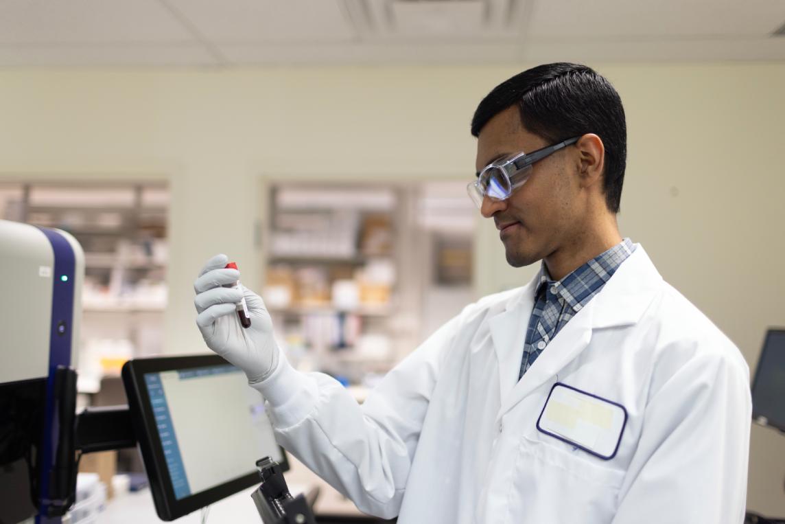 Scientist operating a benchtop flow cytometry instrument touchscreen in the laboratory.