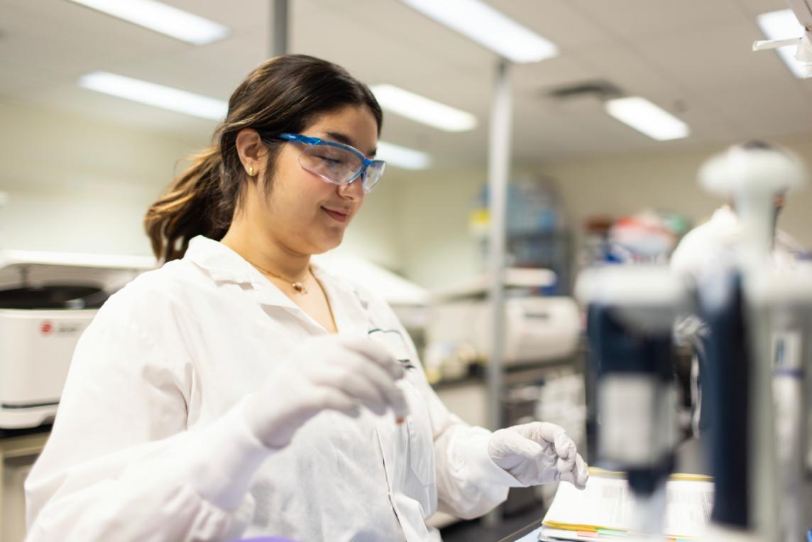 Scientist working at a laboratory bench beside a flow cytometry instrument.