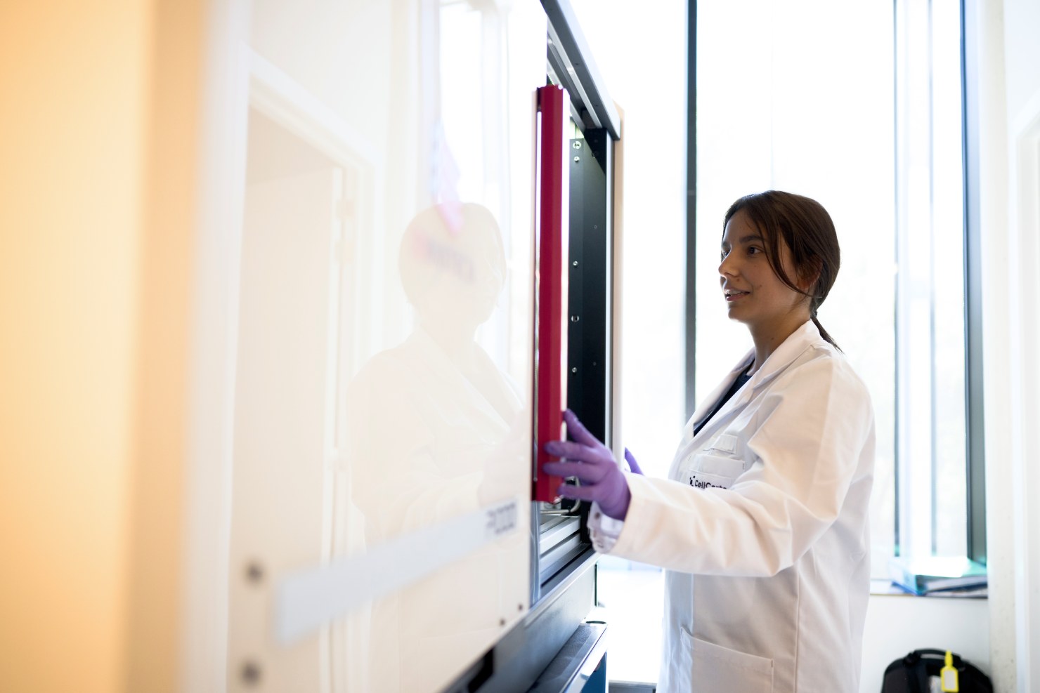 Scientist working beside laboratory instruments by a window for CellCarta late phase clinical trial.