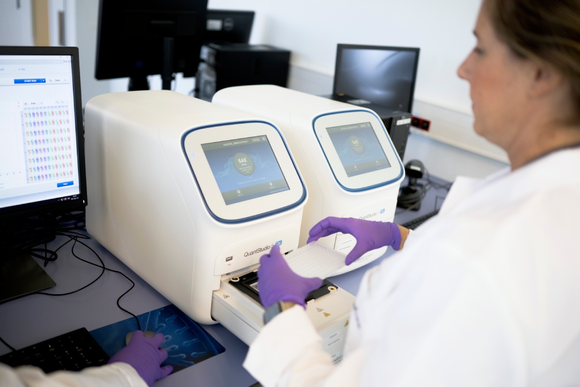 Scientist operating benchtop PCR instrument.