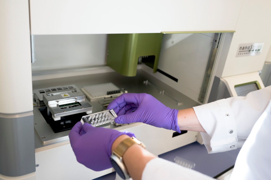 Gloved hands loading samples into a laboratory instrument.