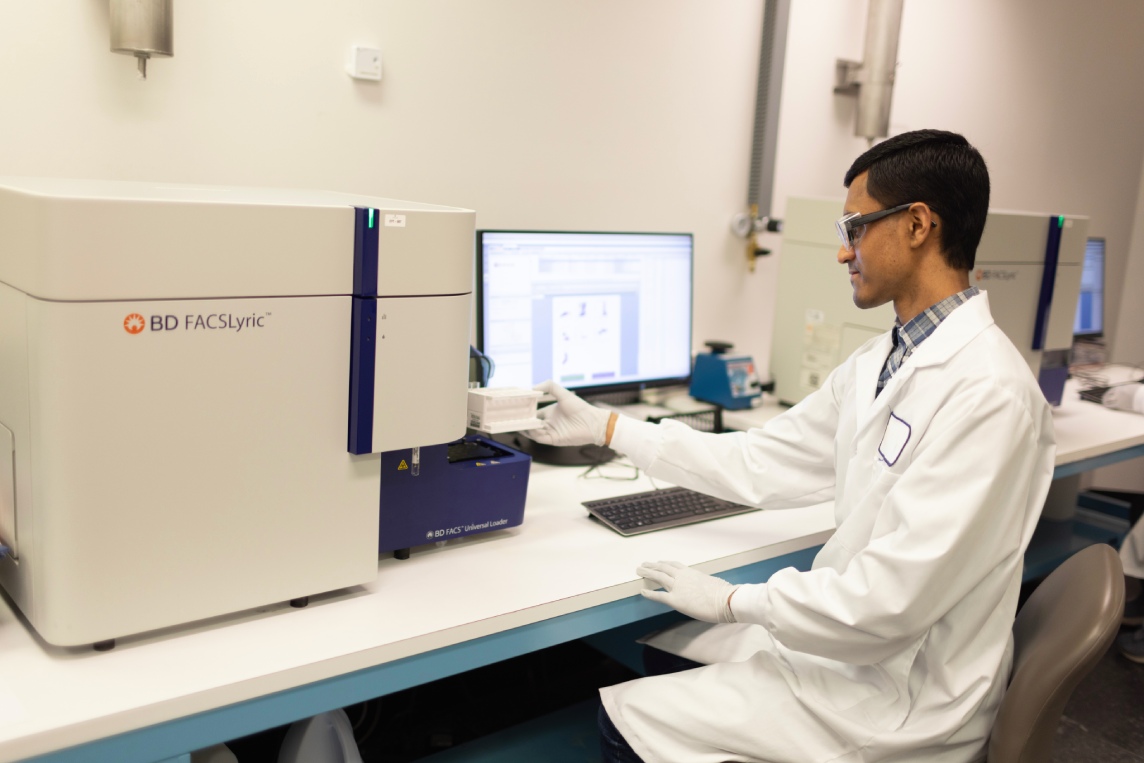 Scientist operating a benchtop flow instrument at a data workstation.