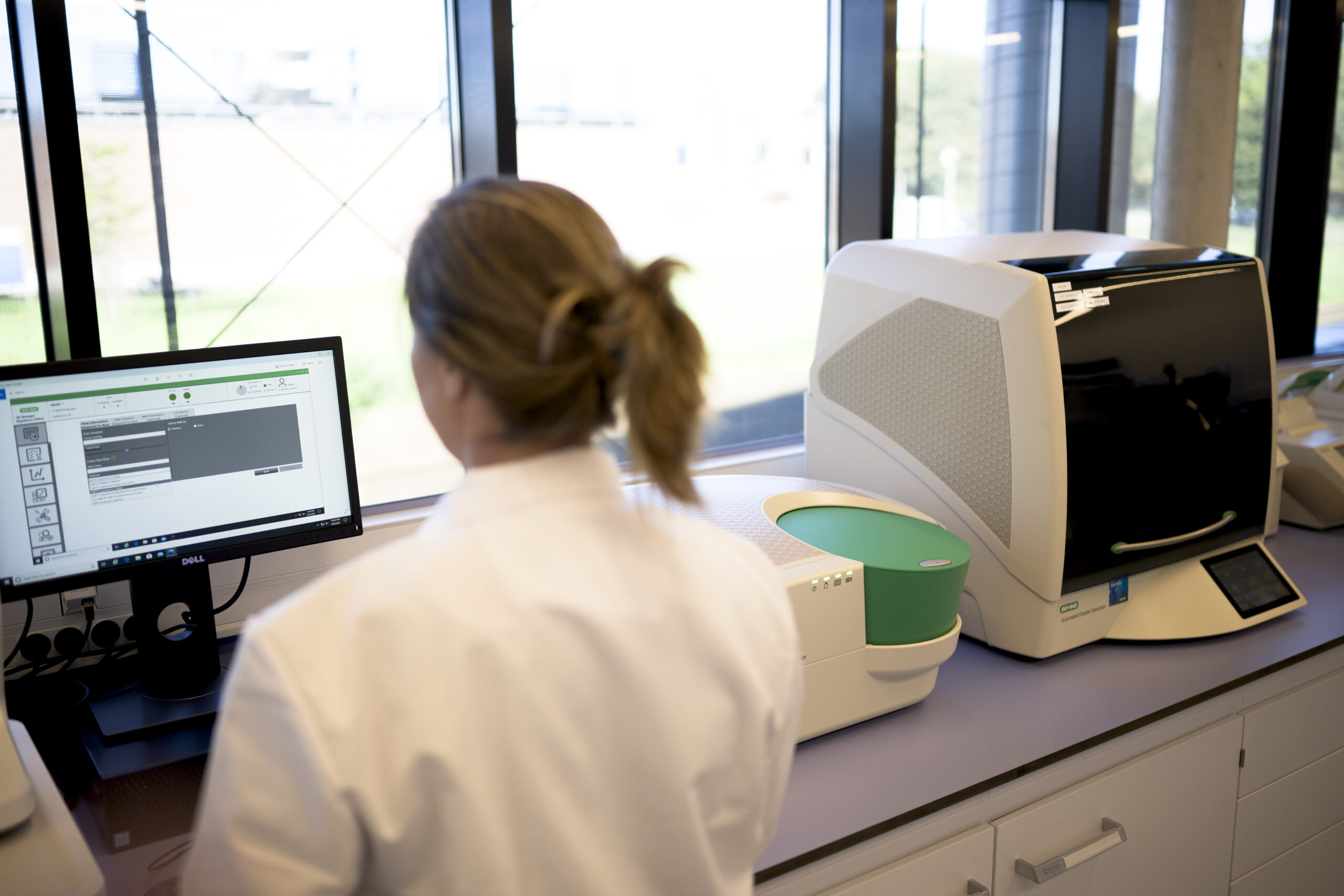 Scientist operating a benchtop dPCR instrument at a data workstation.