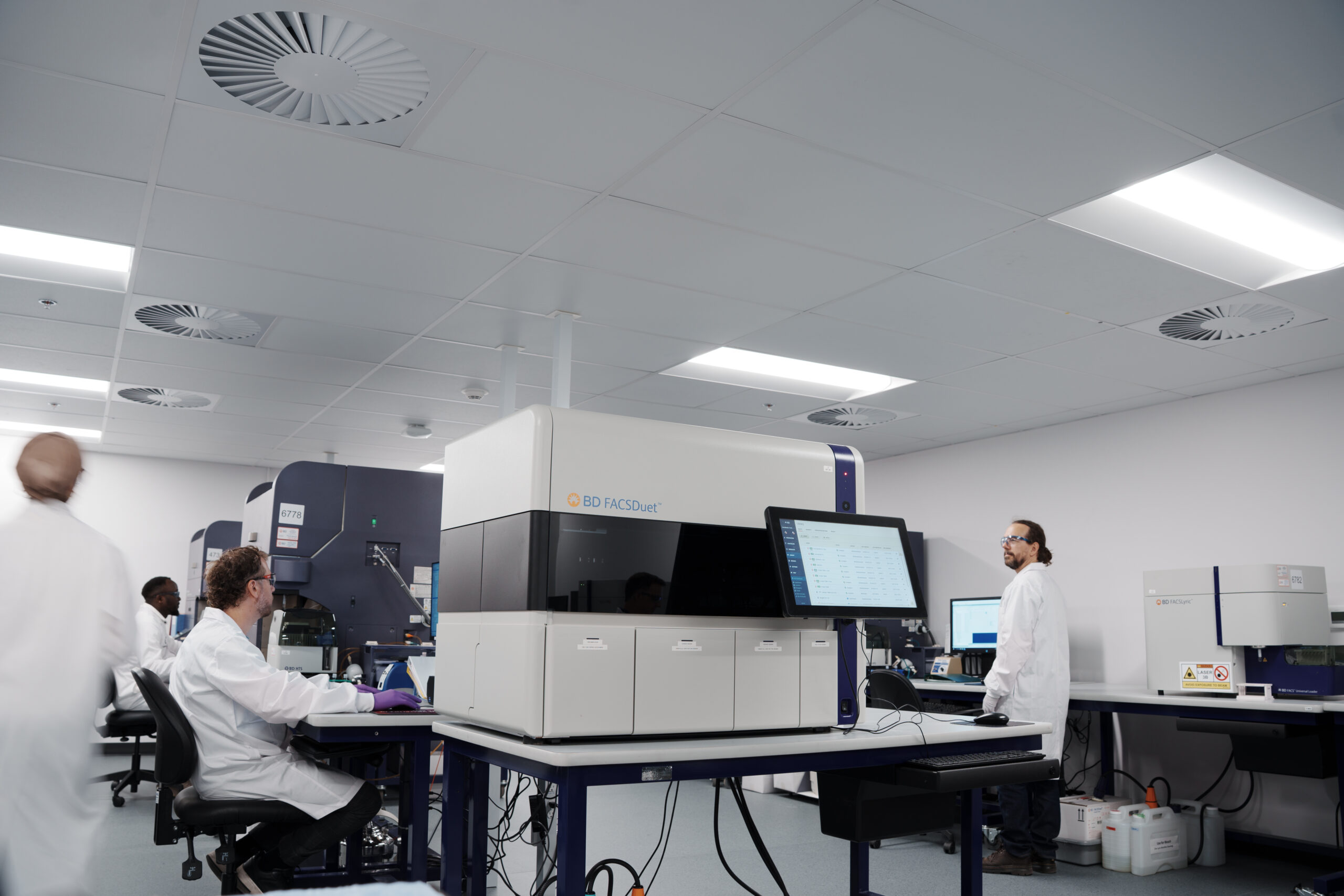 Scientists working with flow cytometry instruments in an open laboratory.