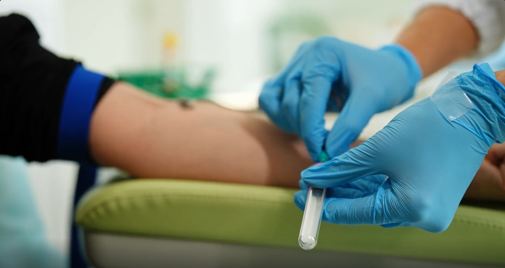 Gloved hand holding a labeled blood sample tube during biospecimen procurement.